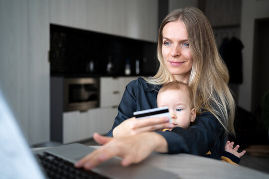 Young Caucasian Mother With Baby Using Laptop And Credit Card For Online Shopping At Home, European Mom Holding Cute Baby On Her Lap