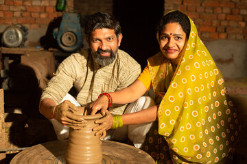 Portrait of happy indian couple pottery maker building clay pot together, woman wearing sari helping her husband,skill india concept. - obrazy, fototapety, plakaty