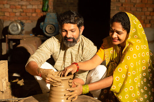 Traditional indian woman pottery maker helping and supporting her husband working with clay pot, skill india concept.