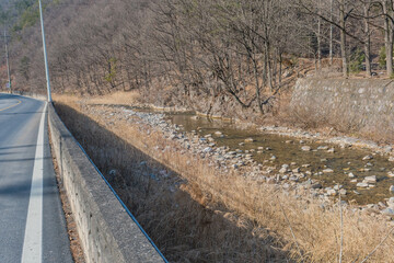 Stream flowing beside country road in woodland mountain countryside.
