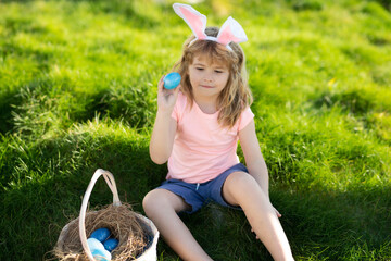 Happy Easter for children. Boy in bunny ears with colorful eggs play and hunting easter eggs outside. Spring holidays.