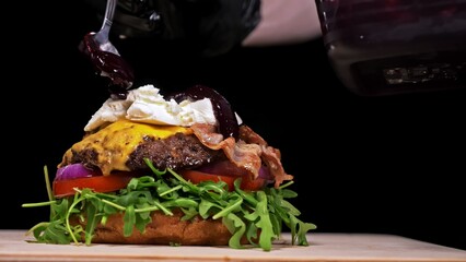 Craft burger is cooking on black background. Consist: sauce, arugula, tomato, red onion, bacon, red currant sauce, ricotta cottage fresh cheese, air bun and marble meat beef. Not made ideal. Looks