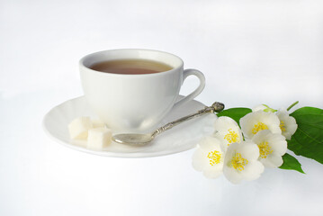Obraz na płótnie Canvas Cup of tea on a saucer, spoon, sugar and jasmine flowers on a white background.