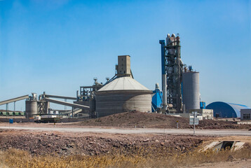 Fototapeta na wymiar Cement plant tower and silos with transporter conveyors on clear blue sky and desert. Mynaral, Kazakhstan.