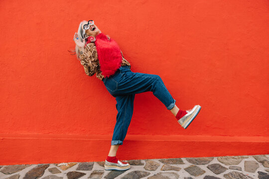 Excited Senior Woman Dancing And Having Fun Against A Red Wall