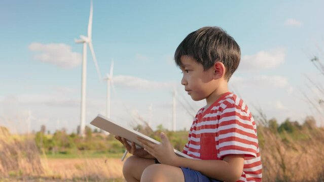 Asian boy child draws pictures and take note on clean energy innovation in windmill farm field.