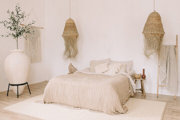 Boho style bedroom interior. Light, warm shades, large bed, straw decorative lamps, large decorative vase, wall panel in Boho style