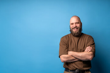 Close up portrait of caucasian bearded man wearing brown t-shirt on blue background. Smiling face. Copy space.