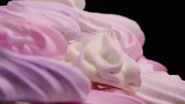 Twirl of sweet meringue rotating on black background. French sweets cookies made from protein and sugar. Close up shot of candy dessert yellow, pink and purple color. Slow motion ready, 4K at 59.94fps