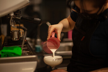 Woman barista pours milk in a cup of coffee in the cafeteria
