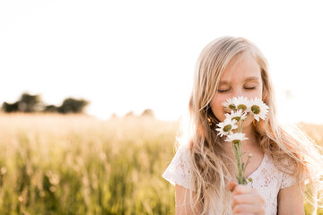 Blond girl smelling flowers in field