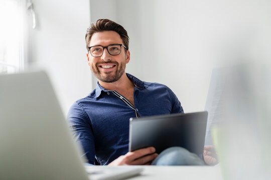 Smiling businessman with tablet PC wearing eyeglasses in office