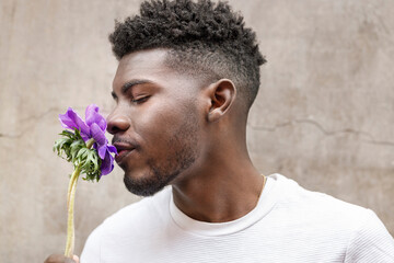 Young man smelling purple flower in front of wall
