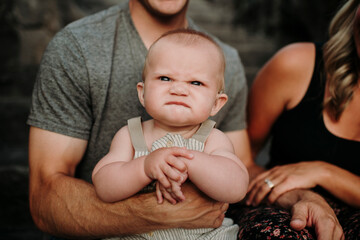 Baby boy making funny face sitting with parents