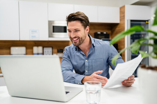 Smiling businessman with document working on laptop at office