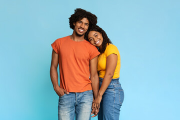 Happy african american couple posing on blue, holding hands