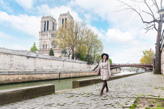Woman walking by river with Notre Dame Cathedral in background on vacation