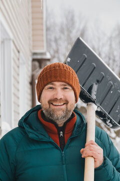 Happy man wearing knit hat carrying snow shovel on shoulder in winter