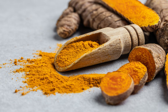 Close-up Turmeric curcumin powder in wooden spoon and fresh curcuma or curcumin on concrete background. Spice, natural coloring, alternative medicine. Long banner format. top view