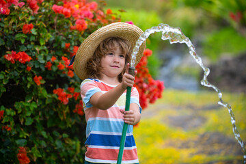 Happy little boy having fun in domestic garden. Child hold watering garden hose. Active outdoors...