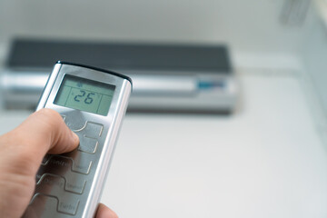 Close-up of a man's hand with a gray remote control pointing at the air conditioner, copy space