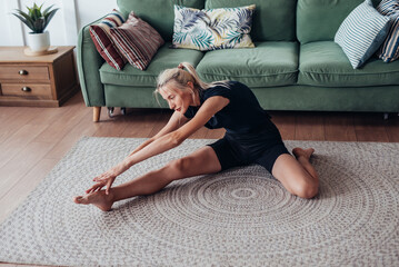 Obraz premium Woman working out at home, doing stretching bends forward while sitting on floor