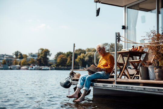Senior man reading newspaper sitting at houseboat on sunny day