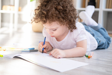 Naklejka premium curly child girl drawing with colored markers lying on floor in living room at home