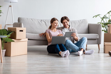 Glad smiling caucasian husband and wife in casual planning new interior with tablet and computer in living room