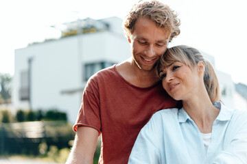 Smiling affectionate couple in front of house