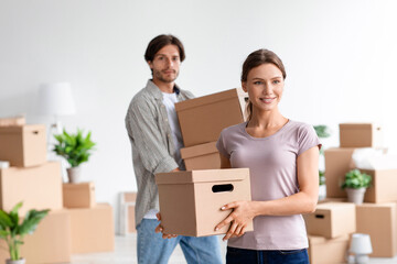 Fototapeta na wymiar Smiling millennial caucasian male and female in casual enjoy moving, carry cardboard boxes with belongings