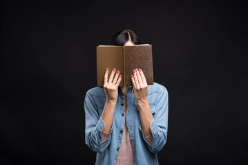 Attractive caucasian brunette girl in a shirt covering her face with a book and reading isolated on...