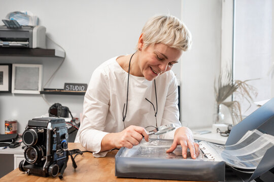 Smiling curator looking photos through magnifying glass on desk at office