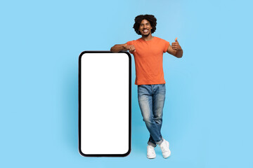 Positive african american guy posing with smartphone with blank screen