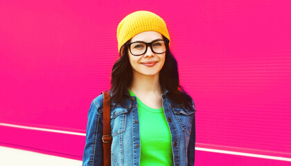 Portrait of modern happy smiling young woman student wearing eyeglasses, yellow hat looking at camera on colorful pink background