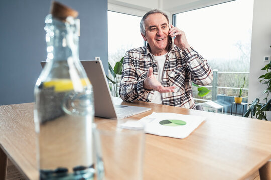 Smiling senior man talking on smart phone sitting at table