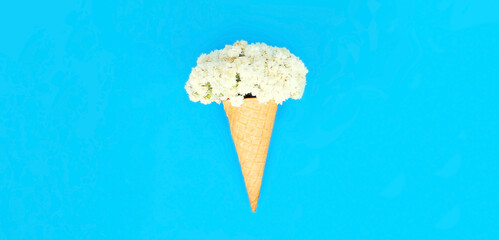 Ice cream cone with flowers on colorful blue background, top view, flat lay