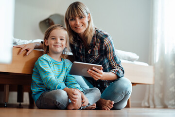 Smiling woman and son with tablet PC in bedroom at home