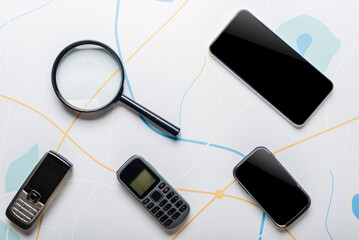Different mobile phones and magnifying glass on the city map background
