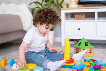 curly child girl playing with pyramid and constructor at home. early children development
