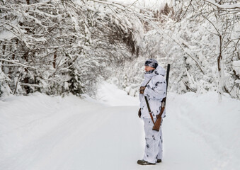 A male hunter stands sideways with a gun on his shoulder in full growth in the winter forest. Concept winter hunting with a gun.