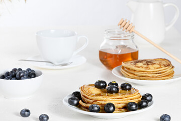 Pancakes with blueberry on white plate, creamer and teacup on white background