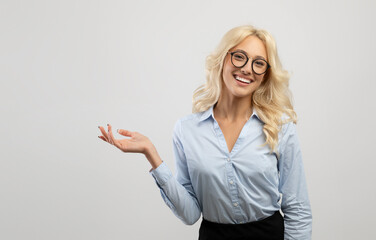 Business offer. Happy blonde businesswoman demonstrating something at her empty palm and smiling at...