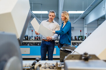 Blond businesswoman discussing over report with businessman in factory