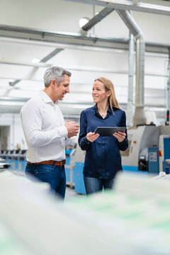 Businessman discussing with blond businesswoman holding tablet PC in factory