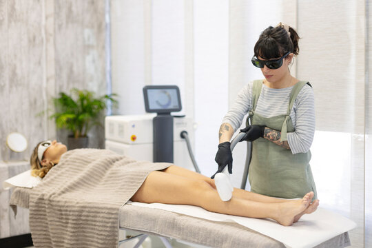 Beautician using hair removal laser machine on woman at aesthetic clinic