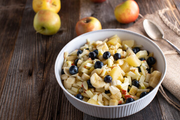 Bowl with fruit salad made with chopped apples, bananas, yellow kiwis and blueberries
