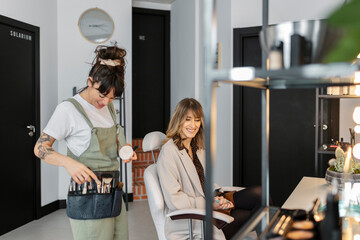 Happy make-up artist talking with customer sitting on chair at salon