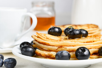 Pancakes with blueberry on white plate, honey and teacup on white table