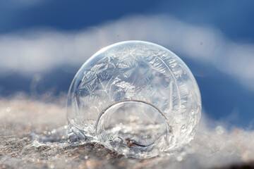 Frozen soap bubble with a beautiful pattern on the snow close-up on a blurry background.